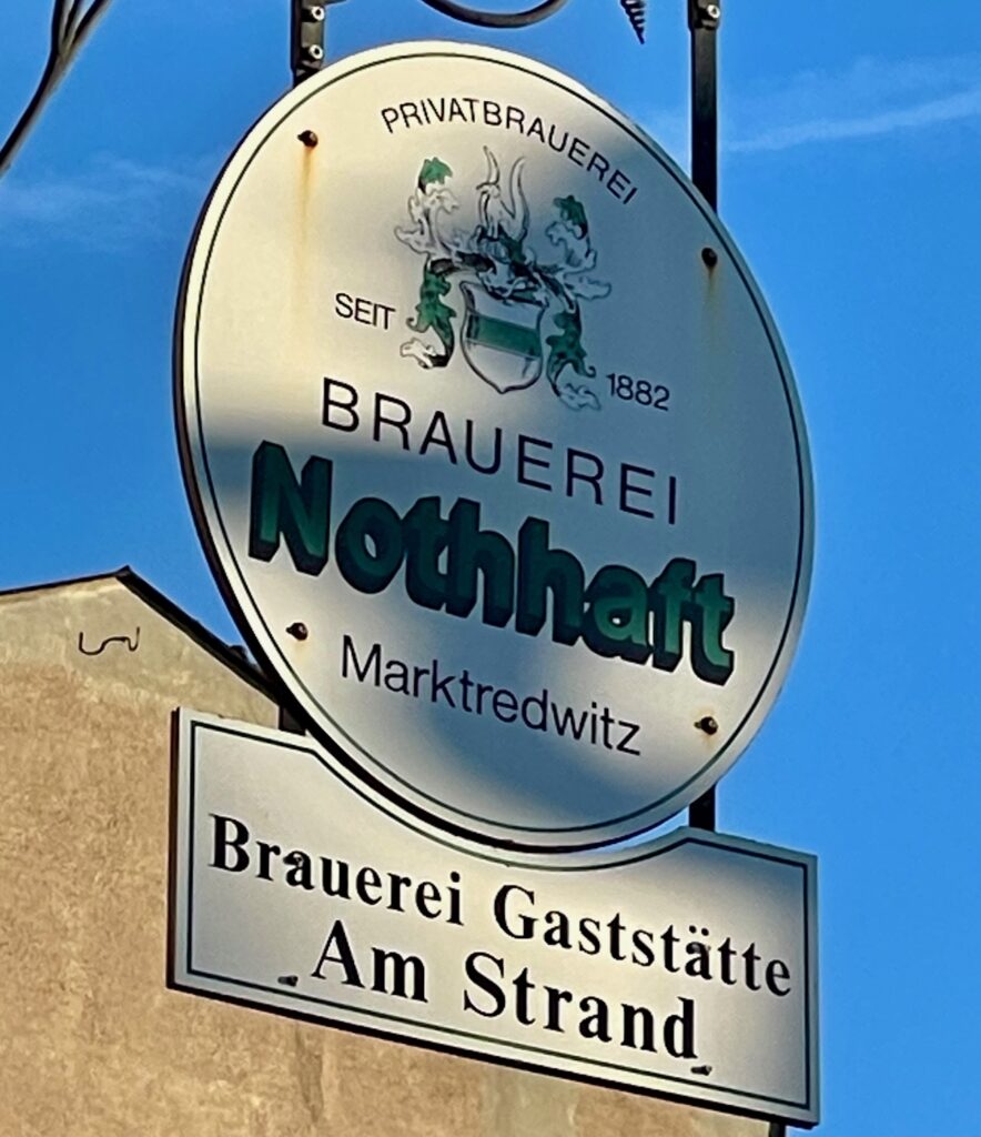Historisches Straßenhinweisschild auf die Brauereigaststätte Am Strand in Marktredwitz mit Brauerei-Nothhaft-Reklame.